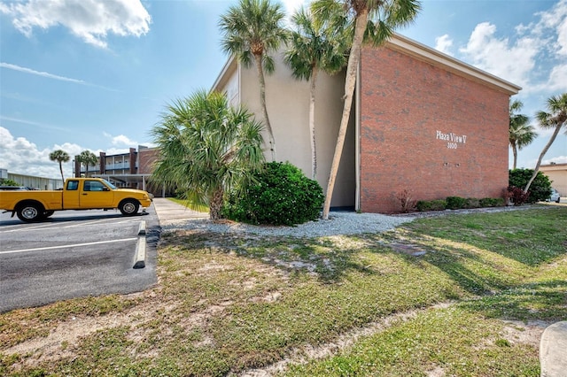 view of side of property with uncovered parking, stucco siding, and a lawn