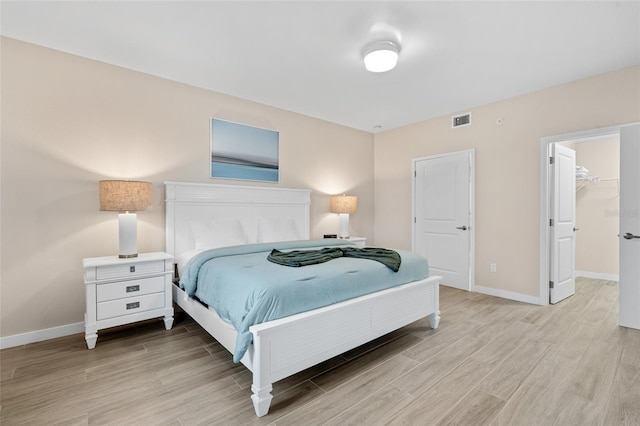 bedroom with baseboards, light wood finished floors, and a walk in closet