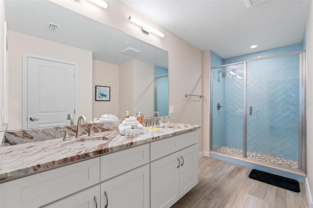 bathroom featuring wood finished floors, a shower stall, and double vanity