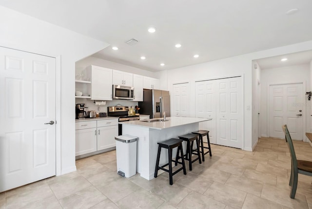 kitchen featuring white cabinets, open shelves, appliances with stainless steel finishes, a kitchen breakfast bar, and a center island with sink