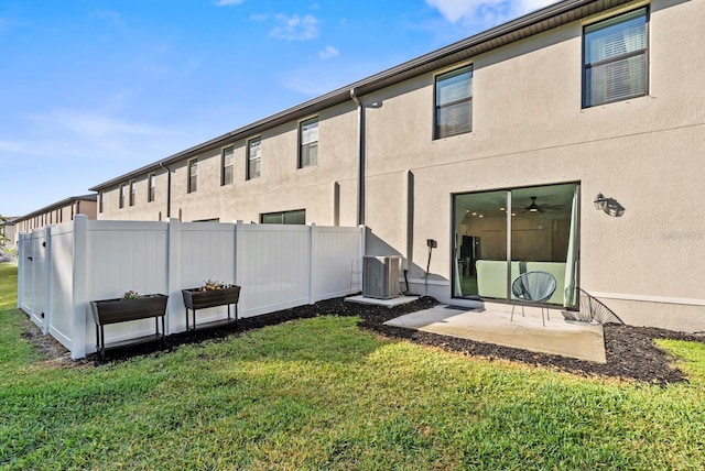 rear view of property featuring stucco siding, central AC unit, fence, and a yard