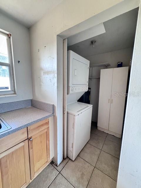 laundry area featuring stacked washer / dryer, a sink, light tile patterned floors, and laundry area
