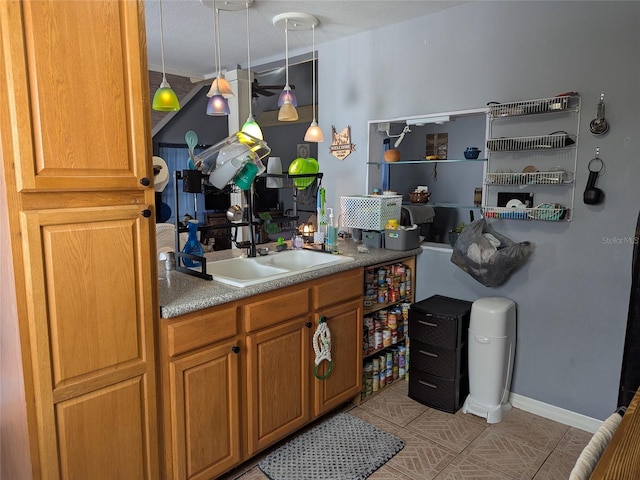 kitchen featuring brown cabinetry, hanging light fixtures, a sink, light tile patterned floors, and baseboards