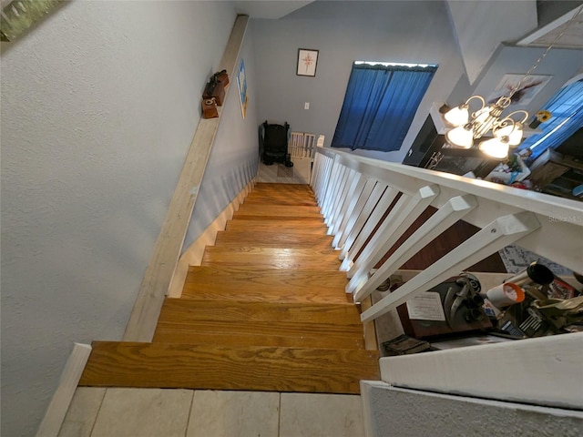 stairs featuring an inviting chandelier, a textured wall, and wood finished floors