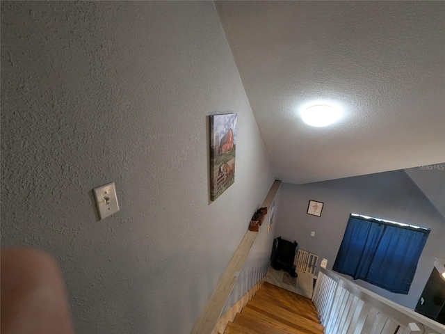 stairway with a textured ceiling, a textured wall, and wood finished floors