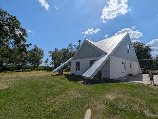 view of side of home with a lawn, metal roof, and a patio