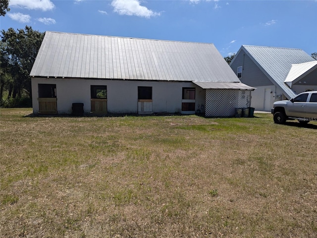 rear view of house featuring a yard, metal roof, and stucco siding