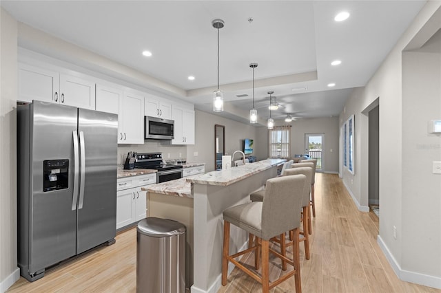 kitchen with stainless steel appliances, a raised ceiling, open floor plan, white cabinets, and a kitchen bar