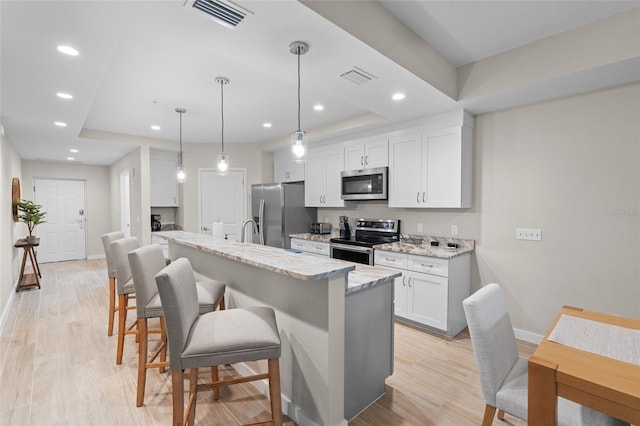kitchen featuring stainless steel appliances, a kitchen bar, baseboards, light wood finished floors, and white cabinetry