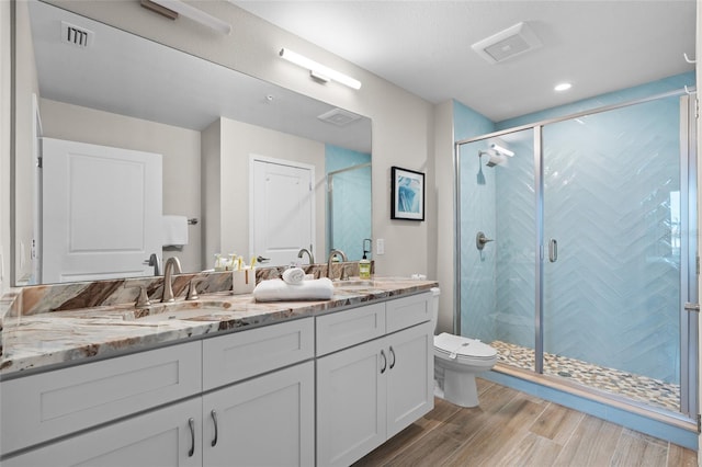 bathroom featuring toilet, wood finished floors, double vanity, and a shower stall