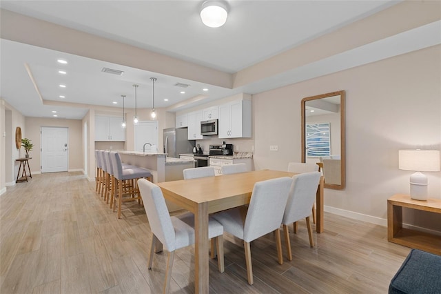 dining space featuring a raised ceiling, light wood finished floors, baseboards, and recessed lighting