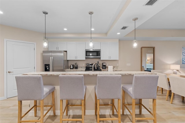 kitchen with appliances with stainless steel finishes, white cabinetry, a center island with sink, a kitchen breakfast bar, and recessed lighting