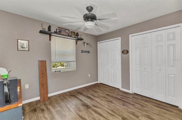 unfurnished bedroom featuring wood finished floors, a ceiling fan, baseboards, and two closets