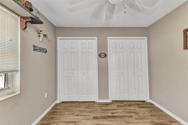 unfurnished bedroom featuring a ceiling fan, baseboards, multiple closets, and wood finished floors