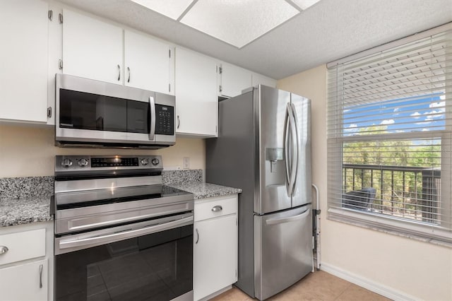 kitchen featuring light stone countertops, light tile patterned floors, baseboards, white cabinets, and stainless steel appliances