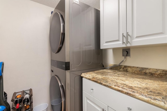 washroom with a textured ceiling, stacked washer and clothes dryer, and cabinet space