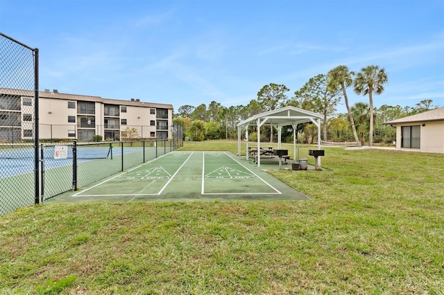 view of home's community with a lawn, fence, a tennis court, and shuffleboard