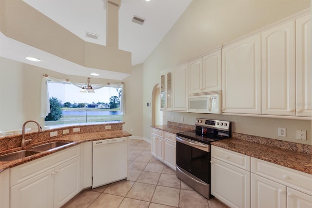 kitchen with a sink, white appliances, dark stone countertops, light tile patterned floors, and visible vents
