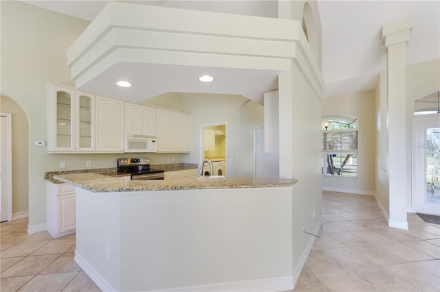 kitchen featuring electric range, light tile patterned flooring, light stone counters, white microwave, and glass insert cabinets