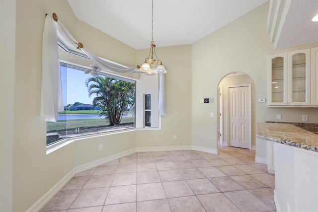 unfurnished dining area featuring arched walkways, lofted ceiling, light tile patterned floors, and a chandelier