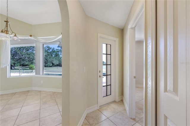doorway with arched walkways, baseboards, and tile patterned flooring