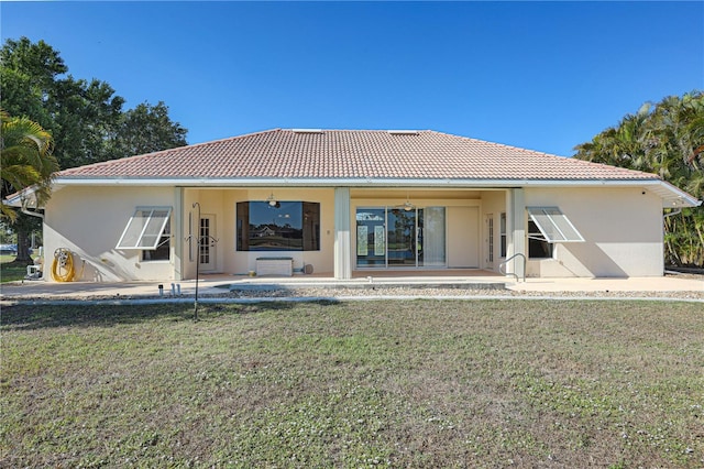 rear view of property with a lawn, a patio, stucco siding, and a tile roof