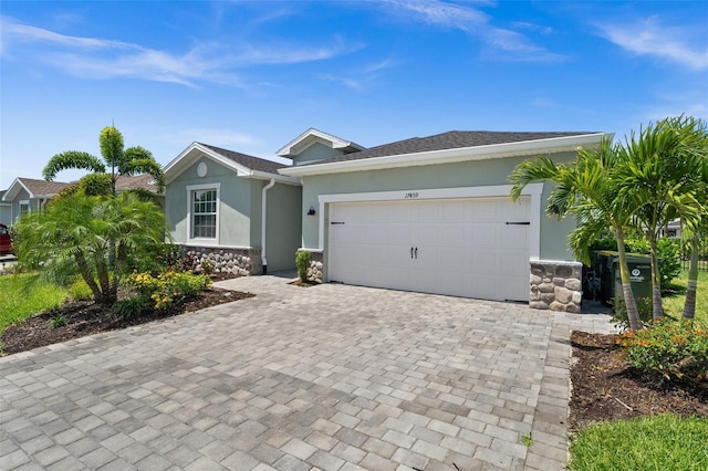 ranch-style home featuring an attached garage, driveway, stone siding, and stucco siding