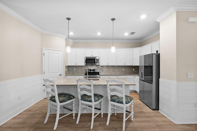 kitchen featuring light stone counters, a wainscoted wall, stainless steel appliances, white cabinetry, and visible vents