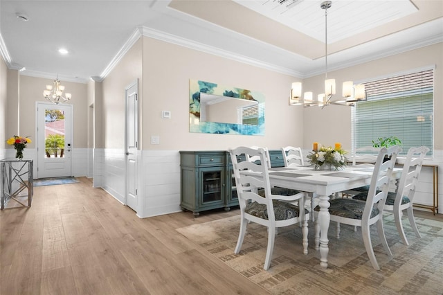 dining room with light wood-style floors, wainscoting, crown molding, and a notable chandelier