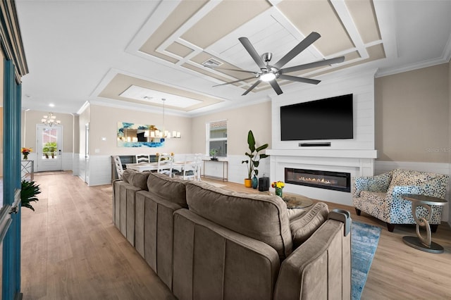 living area with a healthy amount of sunlight, light wood-style floors, a glass covered fireplace, and ceiling fan with notable chandelier