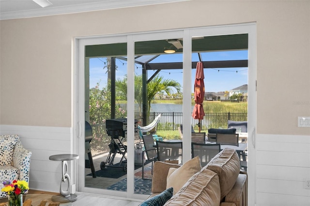doorway featuring a wainscoted wall, a sunroom, wood finished floors, a water view, and ornamental molding