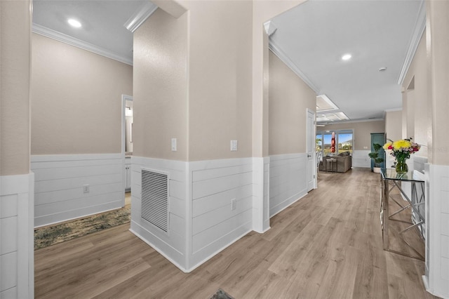 hallway with light wood-style floors, ornamental molding, a wainscoted wall, and visible vents
