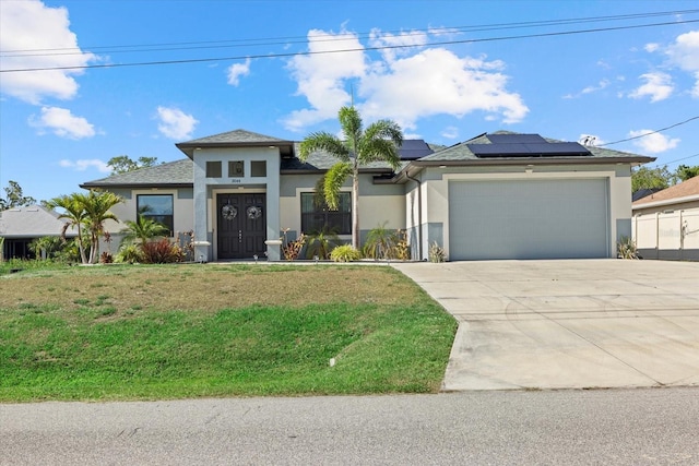 prairie-style house featuring roof mounted solar panels, a front lawn, concrete driveway, an attached garage, and stucco siding