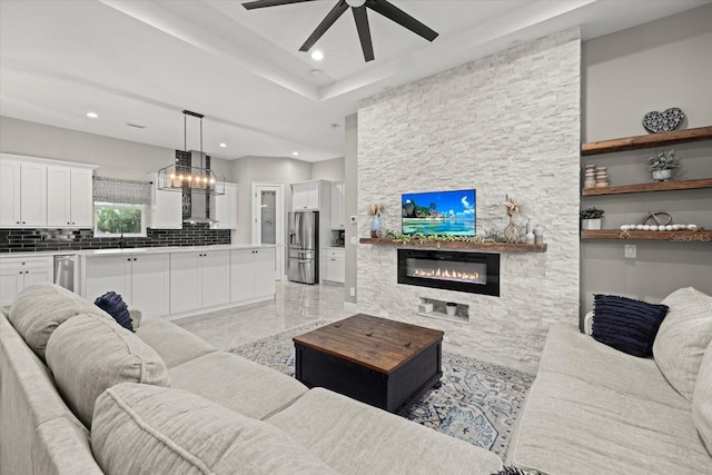 living room featuring recessed lighting, a stone fireplace, and ceiling fan with notable chandelier