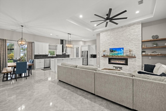living area featuring ceiling fan, a raised ceiling, a stone fireplace, recessed lighting, and visible vents