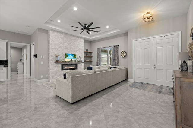 living room with a large fireplace, a tray ceiling, recessed lighting, and marble finish floor