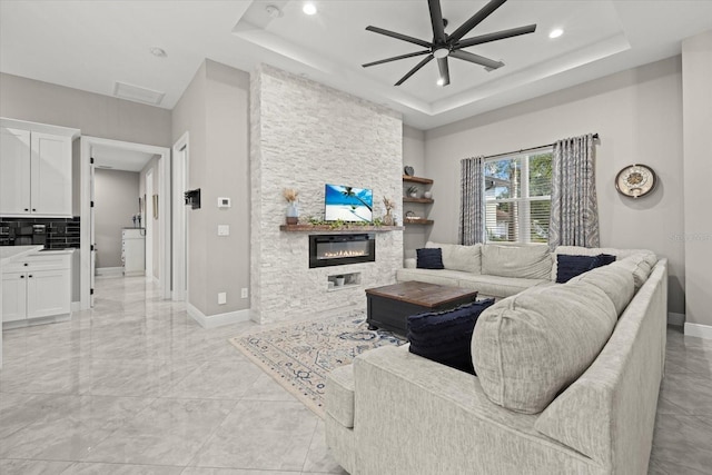 living area with ceiling fan, a large fireplace, a raised ceiling, baseboards, and recessed lighting