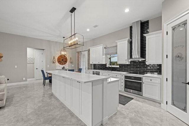 kitchen featuring marble finish floor, appliances with stainless steel finishes, a kitchen island, and wall chimney range hood