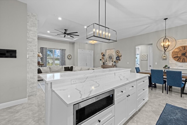 kitchen featuring a kitchen island, open floor plan, white cabinetry, stainless steel microwave, and ceiling fan with notable chandelier