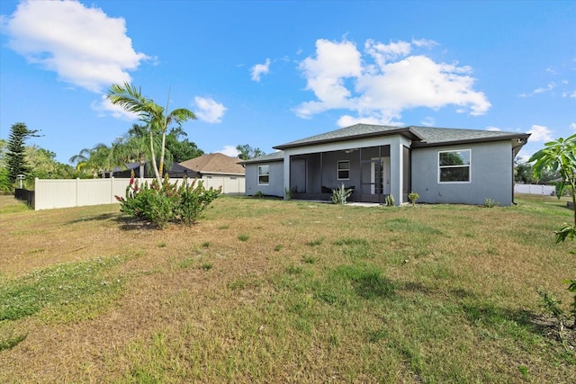 rear view of house featuring a sunroom, a lawn, fence, and stucco siding