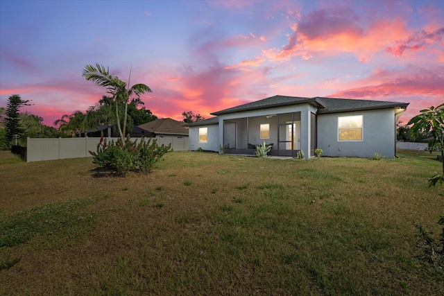 back of house with a lawn, fence, stucco siding, and a sunroom