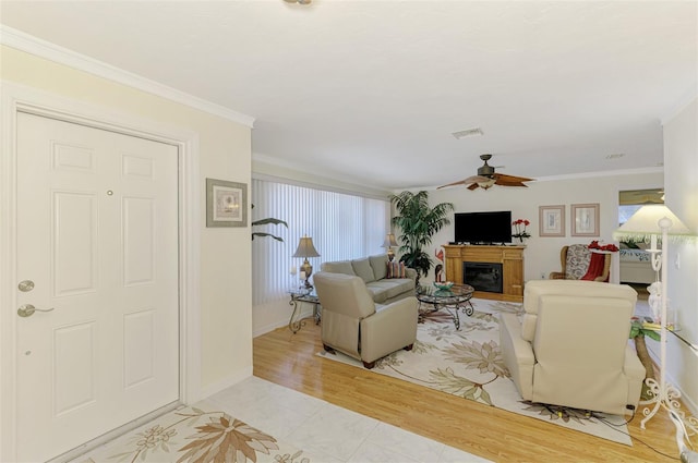 living area with a glass covered fireplace, ceiling fan, ornamental molding, and a healthy amount of sunlight
