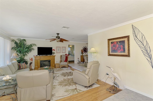 living area with visible vents, a ceiling fan, a glass covered fireplace, and ornamental molding