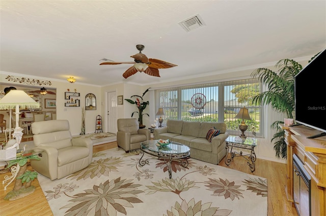 living area featuring a ceiling fan, visible vents, ornamental molding, and light wood finished floors