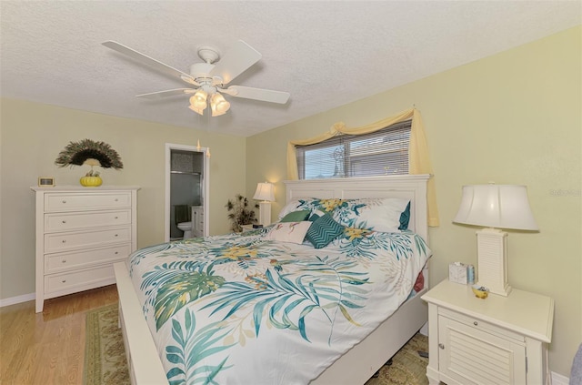 bedroom with ceiling fan, a textured ceiling, baseboards, light wood finished floors, and ensuite bath