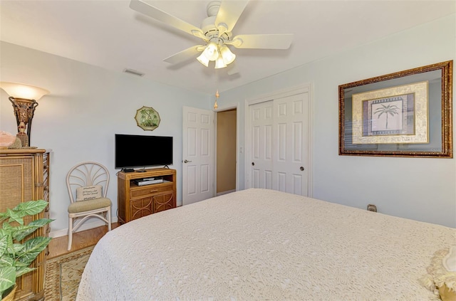 bedroom with ceiling fan, visible vents, wood finished floors, baseboards, and a closet