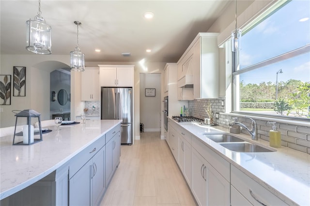 6763 Winding Cypress Dr, Naples, FL 34114 - kitchen featuring pendant lighting, white cabinetry, light stone counters, a sink, and appliances with stainless steel finishes