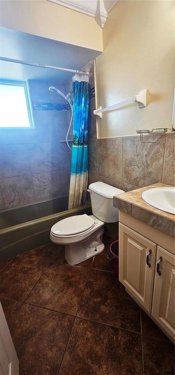570 Mimosa Ave NW, Port Charlotte, FL 33952 - bathroom featuring vanity, toilet, shower / tub combo with curtain, tile patterned floors, and tile walls