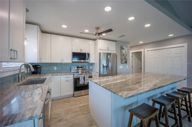 kitchen with a sink, stainless steel appliances, white cabinets, decorative backsplash, and light stone counters
