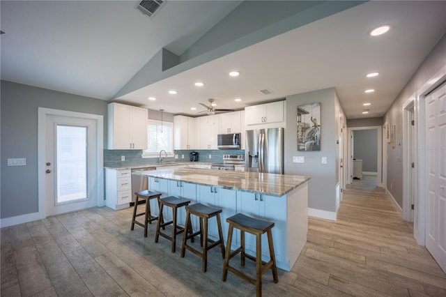 kitchen featuring light wood-style flooring, stainless steel appliances, a kitchen breakfast bar, white cabinets, and visible vents